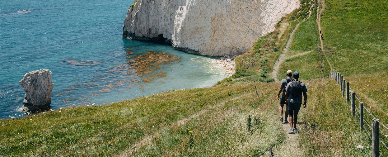 A man hiking on a grassy cliff near the sea.