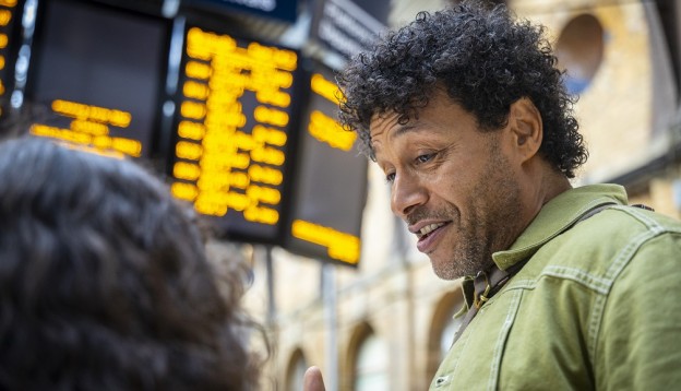 Man talking to daughter in front of departures board at train station